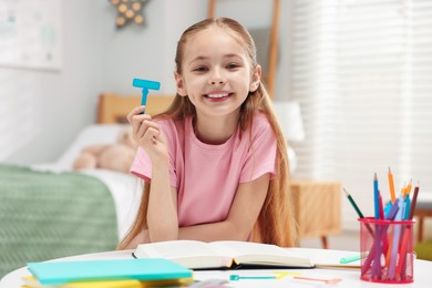 Photo of Dyslexia. Little girl holding letter T at table indoors