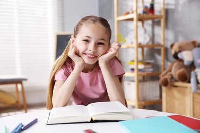 Photo of Dyslexia. Little girl reading book at table indoors