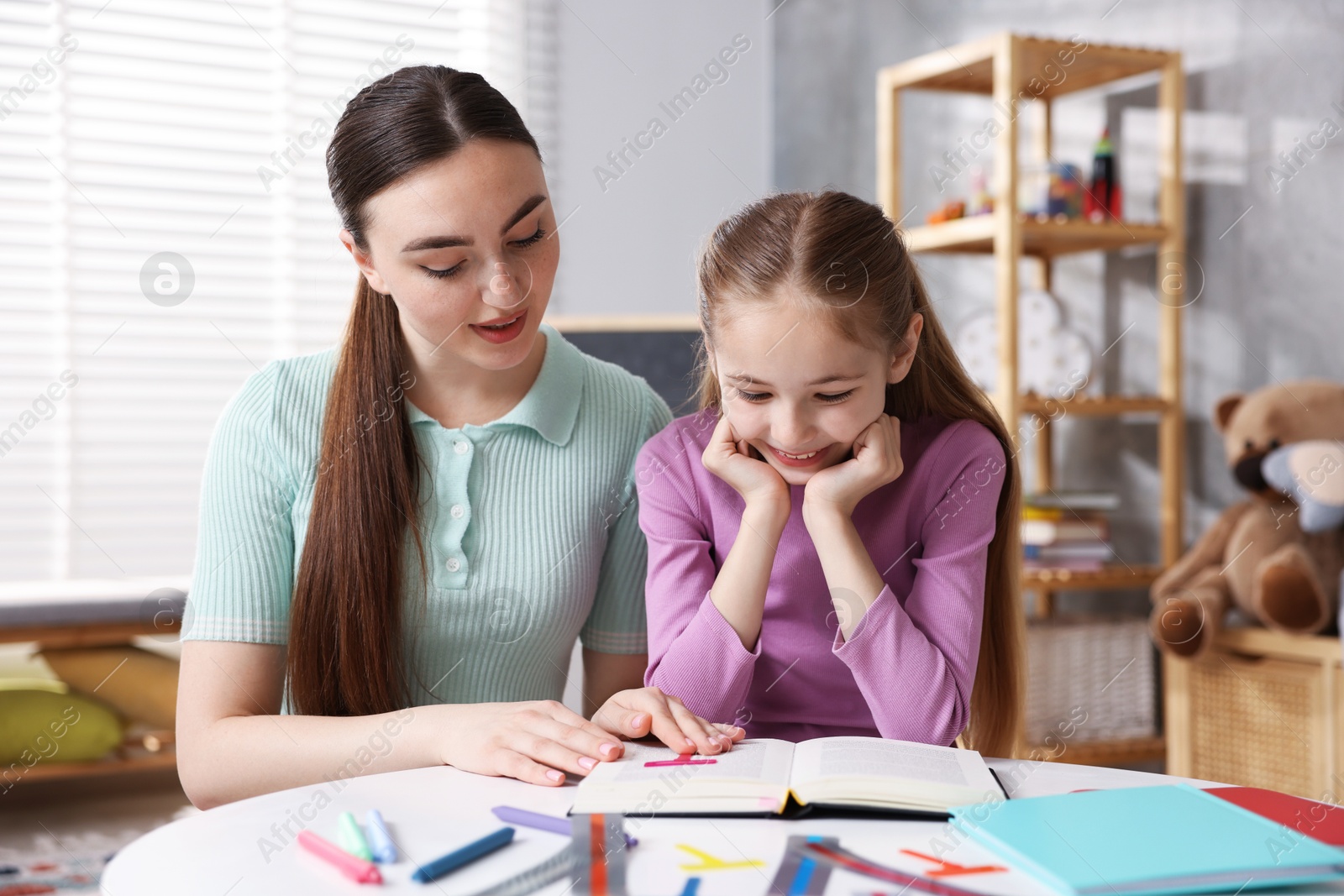 Dyslexia. Mother and her daughter reading book at table indoors Photo of Dyslexia. Mother and her daughter reading book at table indoors