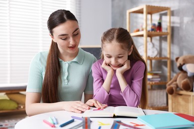 Photo of Dyslexia. Mother and her daughter reading book at table indoors