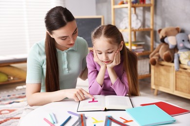 Photo of Dyslexia. Mother and her upset daughter reading book at table indoors