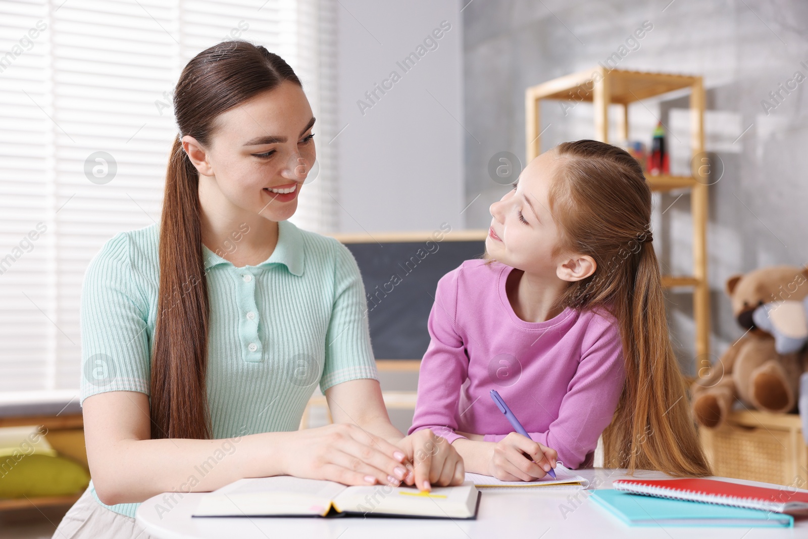 Dyslexia. Mother with her daughter reading book and writing at table indoors Photo of Dyslexia. Mother with her daughter reading book and writing at table indoors