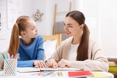 Photo of Dyslexia. Mother and her daughter reading book at table indoors