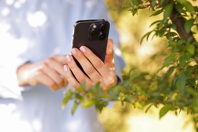 Photo of Woman using plant recognition application on smartphone outdoors, closeup