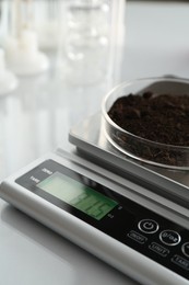 Photo of Scale with Petri dish of sample on white mirror table, closeup