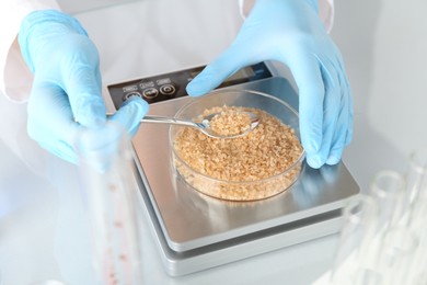 Photo of Scientist weighing Petri dish with sample on scales at white mirror table, closeup