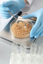 Photo of Scientist weighing Petri dish with sample on scales at white mirror table, closeup
