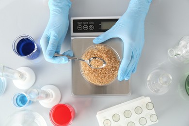 Photo of Scientist weighing Petri dish with sample on scales at white table, top view