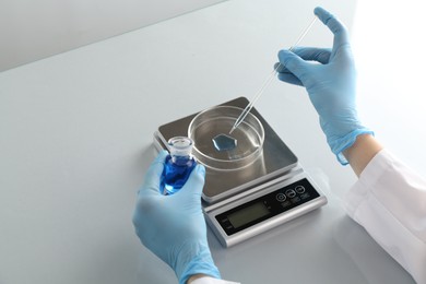 Photo of Scientist working with samples and scales at white mirror table in laboratory, closeup