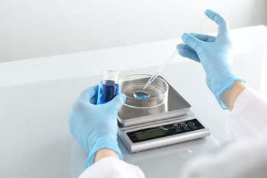 Photo of Scientist working with samples and scales at white mirror table in laboratory, closeup