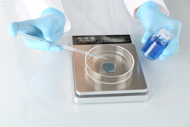 Photo of Scientist working with samples and scales at white mirror table in laboratory, closeup