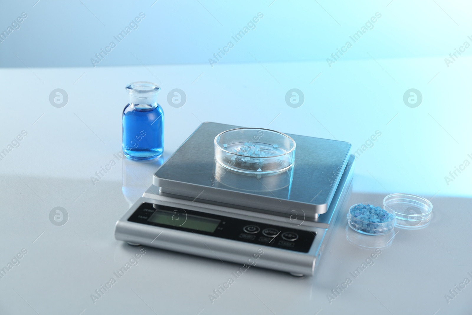Scale with Petri dish of sample and other laboratory glassware on white table in color lights, closeup Photo of Scale with Petri dish of sample and other laboratory glassware on white table in color lights, closeup