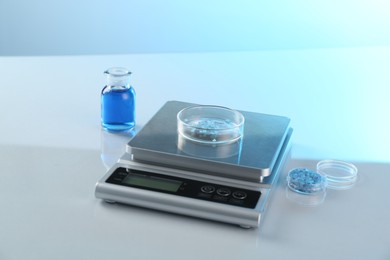 Photo of Scale with Petri dish of sample and other laboratory glassware on white table in color lights, closeup