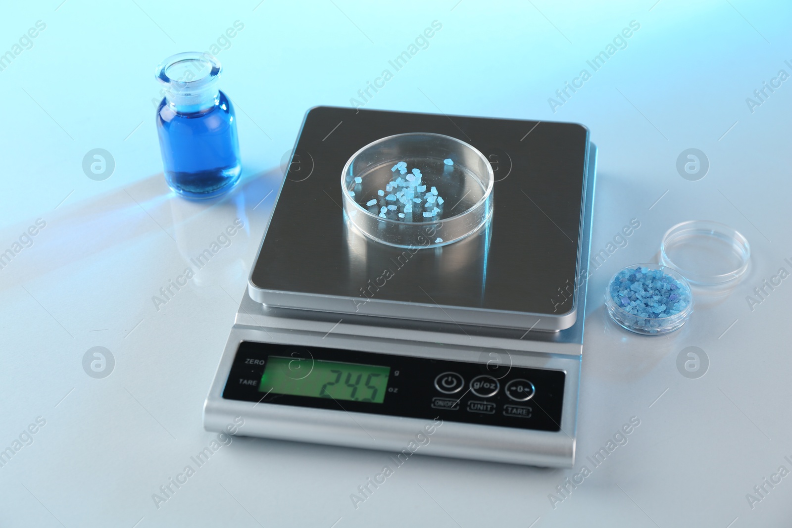 Scale with Petri dish of sample and other laboratory glassware on white table in color lights, closeup Photo of Scale with Petri dish of sample and other laboratory glassware on white table in color lights, closeup
