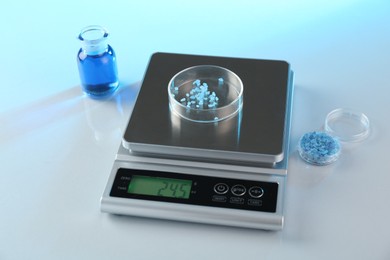 Photo of Scale with Petri dish of sample and other laboratory glassware on white table in color lights, closeup