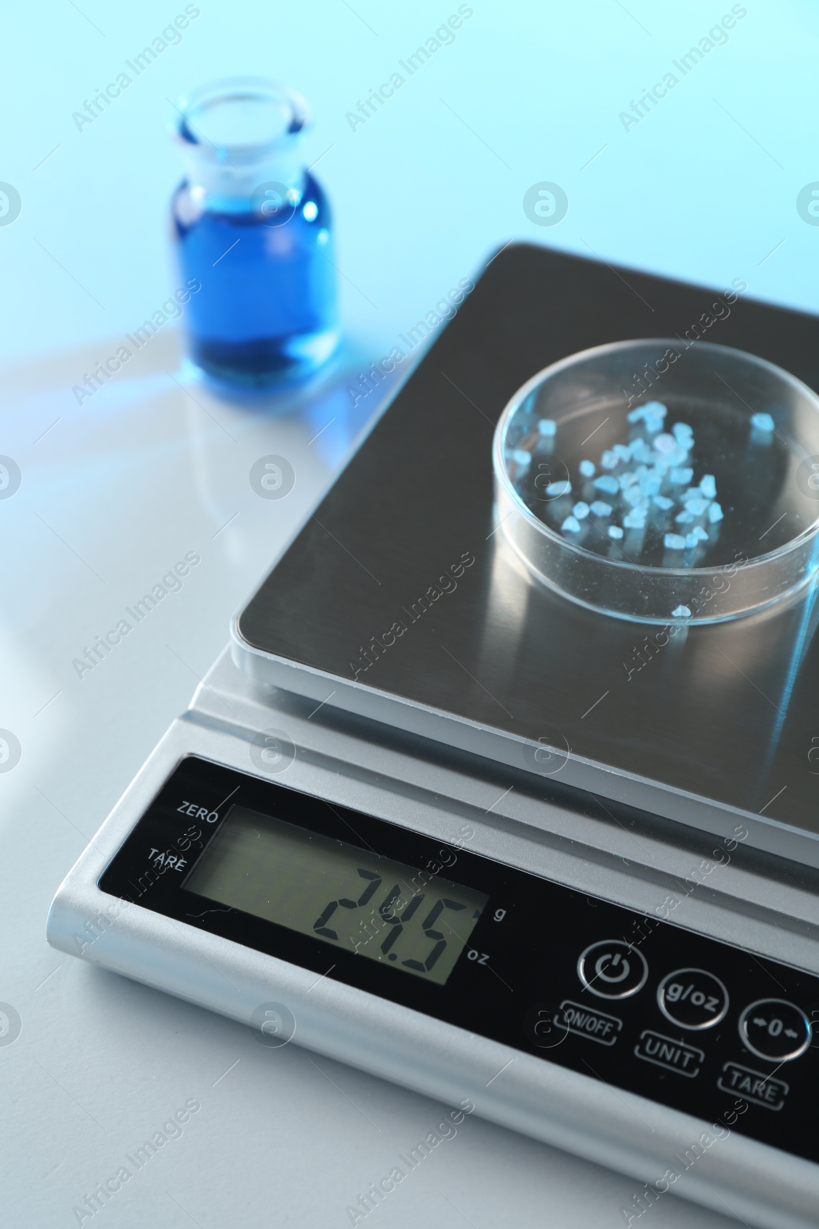 Scale with Petri dish of sample and other laboratory glassware on white table in color lights, closeup Photo of Scale with Petri dish of sample and other laboratory glassware on white table in color lights, closeup