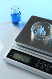 Photo of Scale with Petri dish of sample and other laboratory glassware on white table in color lights, closeup