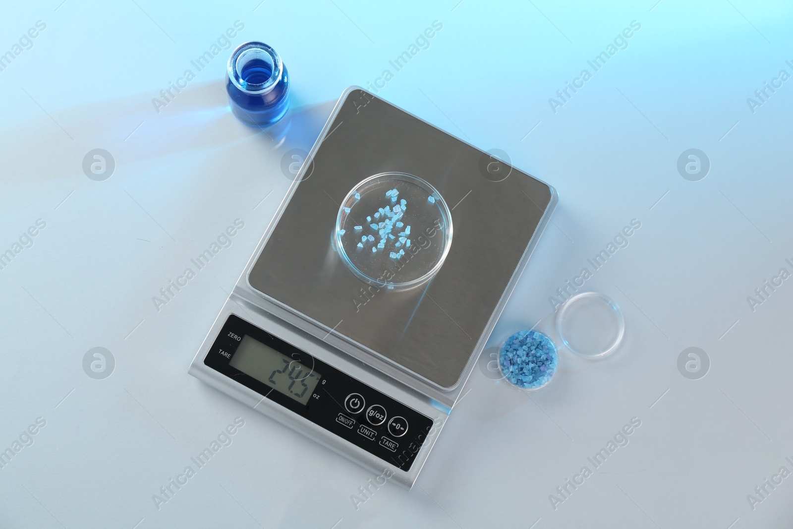 Scale with Petri dish of sample and other laboratory glassware on white table in color lights, flat lay Photo of Scale with Petri dish of sample and other laboratory glassware on white table in color lights, flat lay