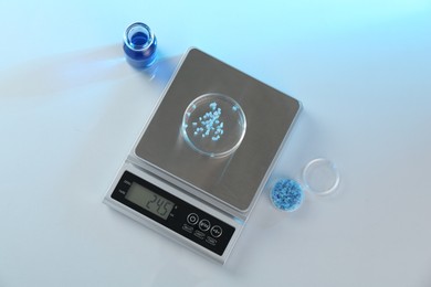 Photo of Scale with Petri dish of sample and other laboratory glassware on white table in color lights, flat lay