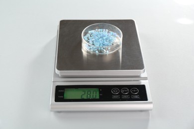 Photo of Scale with Petri dish of sample on white mirror table, closeup