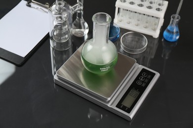 Photo of Scale with flask of sample and other laboratory glassware on black mirror table