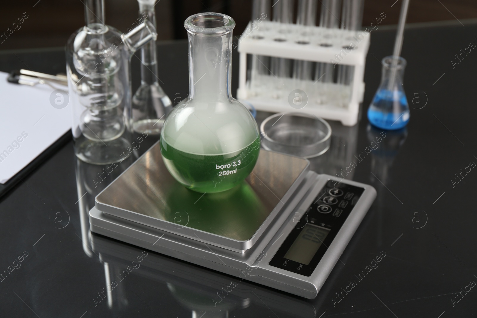 Scale with flask of sample and other laboratory glassware on black mirror table, closeup Photo of Scale with flask of sample and other laboratory glassware on black mirror table, closeup