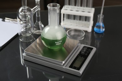 Photo of Scale with flask of sample and other laboratory glassware on black mirror table, closeup