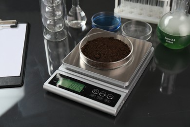 Photo of Scale with Petri dish of sample and other laboratory glassware on black mirror table, closeup