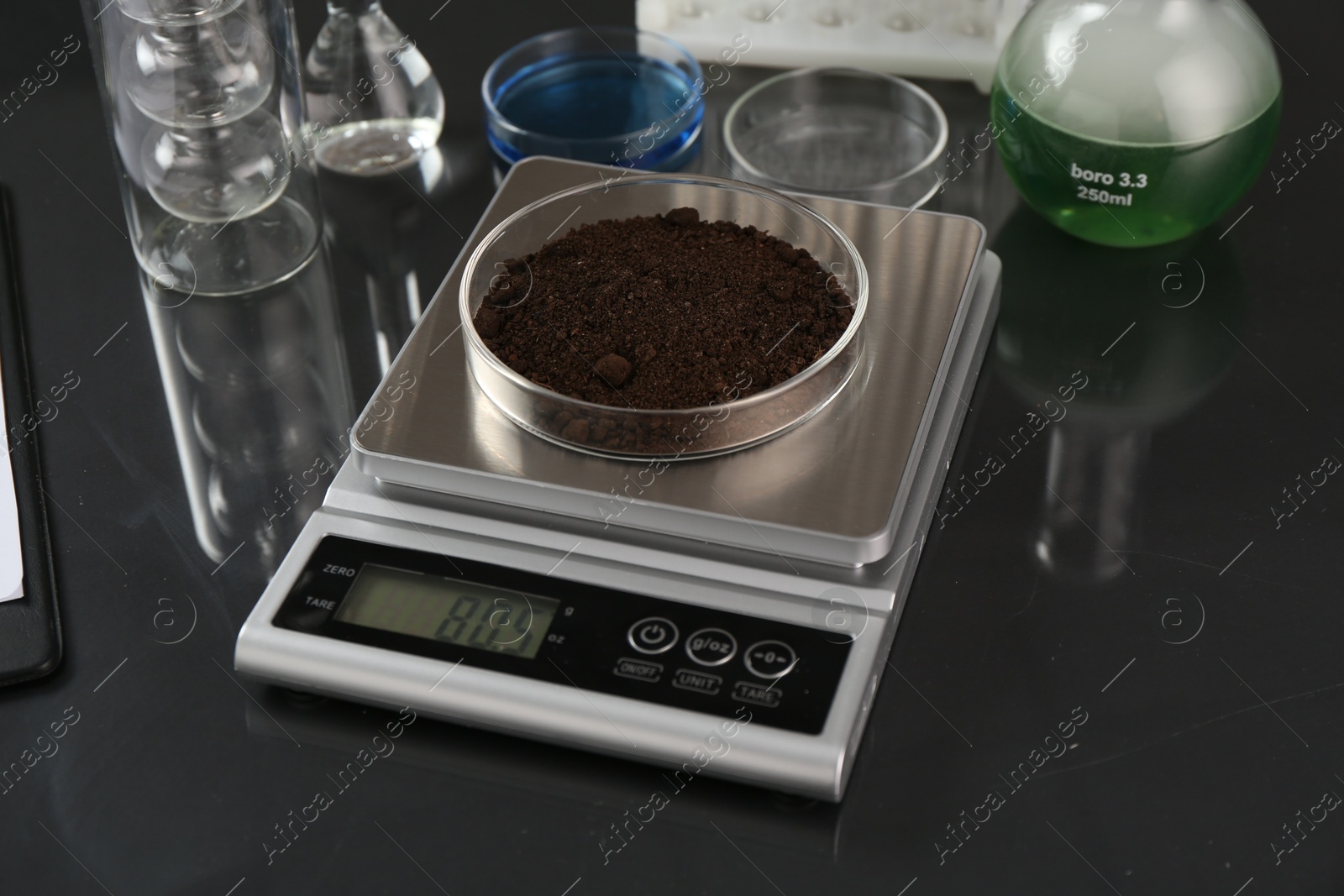 Scale with Petri dish of sample and other laboratory glassware on black mirror table, closeup Photo of Scale with Petri dish of sample and other laboratory glassware on black mirror table, closeup
