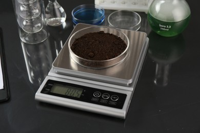 Photo of Scale with Petri dish of sample and other laboratory glassware on black mirror table, closeup