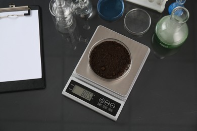 Photo of Scale with Petri dish of sample and other laboratory glassware on black mirror table, flat lay