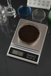 Photo of Scale with Petri dish of sample and other laboratory glassware on black mirror table, above view