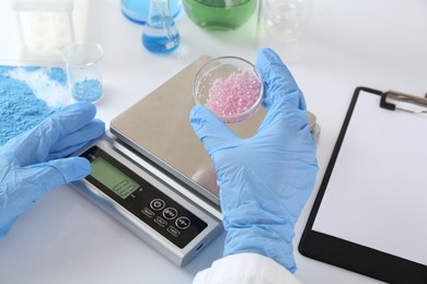 Photo of Scientist working with Petri dish of sample and scales at white table, closeup