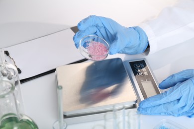 Photo of Scientist working with Petri dish of sample and scales at white table, closeup