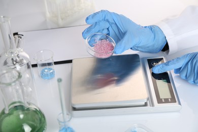 Photo of Scientist working with Petri dish of sample and scales at white table, closeup