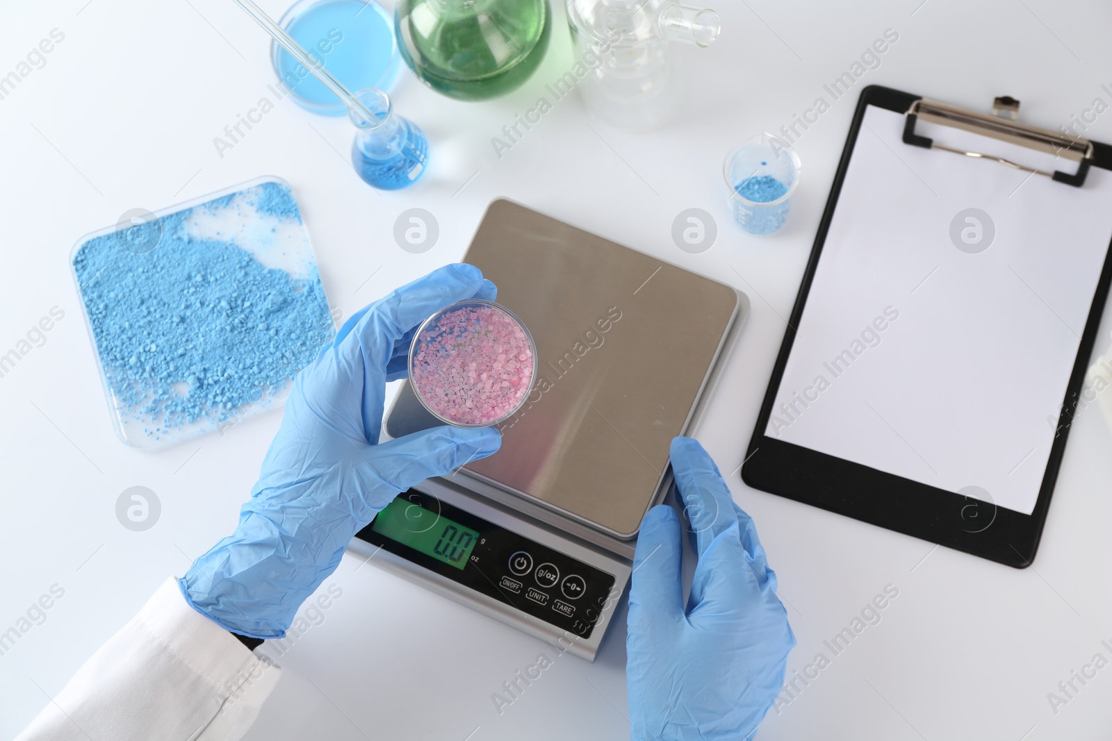 Scientist working with Petri dish of sample and scales at white table, top view Photo of Scientist working with Petri dish of sample and scales at white table, top view