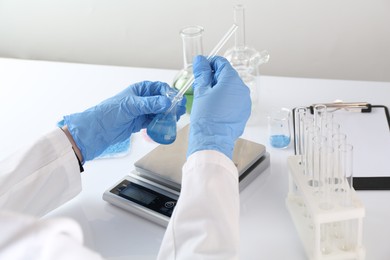 Photo of Scientist working with sample and scales at white table, closeup