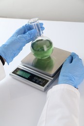 Photo of Scientist weighing sample on scales at white table, closeup