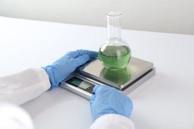 Photo of Scientist weighing sample on scales at white table, closeup
