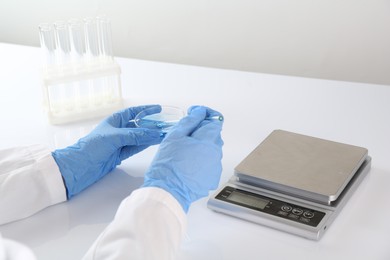 Photo of Scientist working with sample near scales at white table, closeup