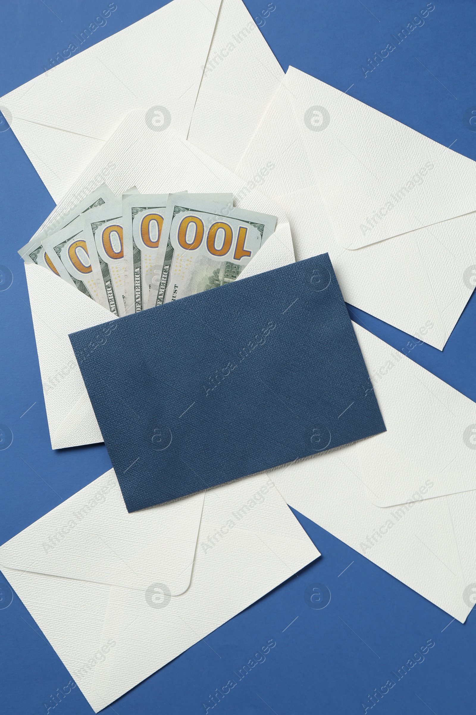 Photo of Money bonus. Envelopes with dollar banknotes on blue background, flat lay
