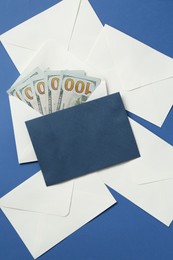 Photo of Money bonus. Envelopes with dollar banknotes on blue background, flat lay