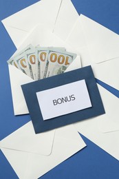 Photo of Envelopes with word Bonus and money on blue background, flat lay