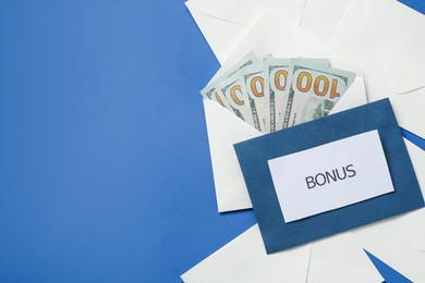 Photo of Envelopes with word Bonus and money on blue background, flat lay. Space for text