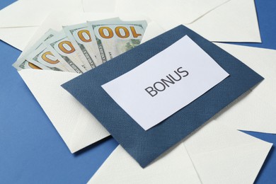Photo of Envelopes with word Bonus and money on blue background, closeup