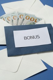 Photo of Envelopes with word Bonus and money on blue background, closeup