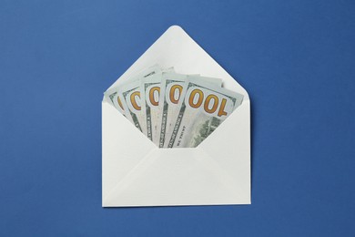 Photo of Money bonus. Envelope with dollar banknotes on blue background, top view