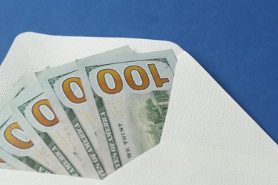 Photo of Money bonus. Envelope with dollar banknotes on blue background, closeup