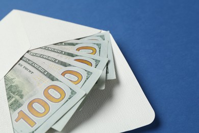 Photo of Money bonus. Envelope with dollar banknotes on blue background, closeup