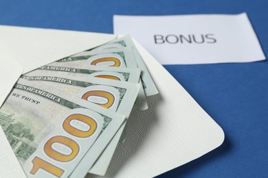 Photo of Envelope with money and word Bonus on blue background, closeup